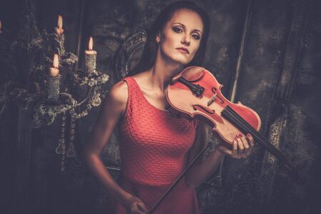 Young woman in red dress playing violin in mystic interior の写真素材