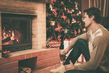 Man with cup of hot drink near fireplace in Christmas decorated houseの写真素材