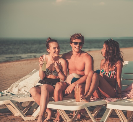Group of multi ethnic friends sunbathing on a deck chairs on a beachの写真素材