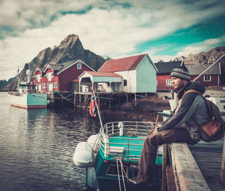 Man traveller sitting on a pier in Reine village, Norwayの写真素材