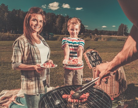 Young family preparing sausages on a grill outdoorsの写真素材