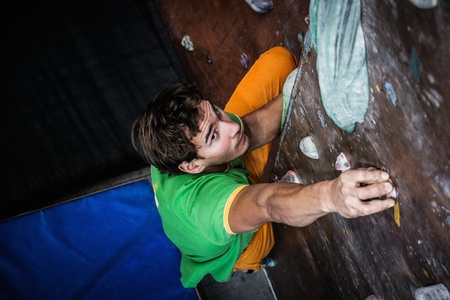 Muscular man practicing rock-climbing on a rock wall indoorsの写真素材