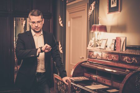 Middle-aged man looking at his wrist watch in luxury vintage style interiorの写真素材