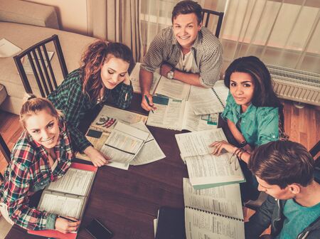 Multi ethnic group of students preparing for exams in home interior behind table