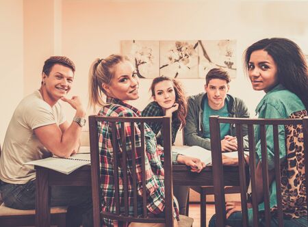 Multi ethnic group of students preparing for exams in home interior behind table