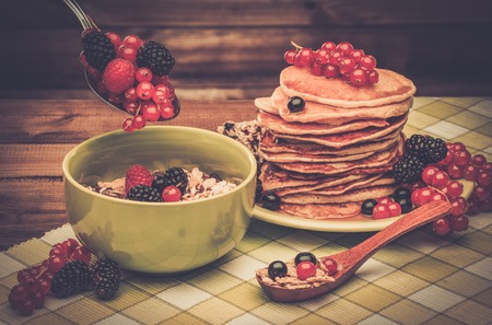 Healthy breakfast with pancakes, fresh berries and muesli on tablecloth in rural interior