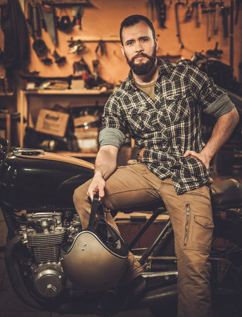 Rider and his vintage style cafe-racer motorcycle in customs garageの写真素材