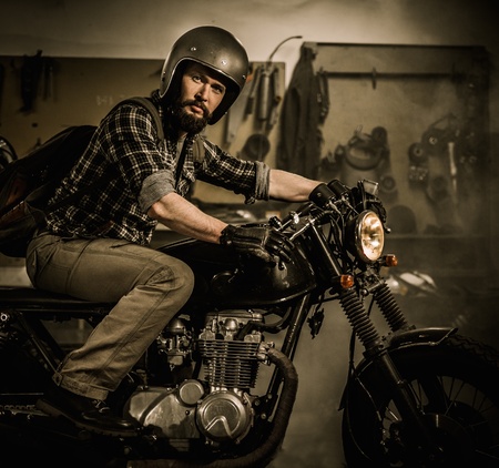 Rider and his vintage style cafe-racer motorcycle in customs garageの写真素材