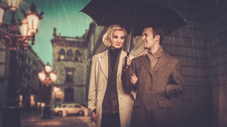 Elegant couple with umbrella walking outdoors in the rain