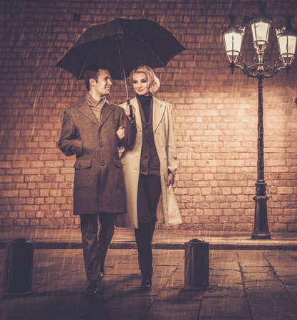 Elegant couple with umbrella walking outdoors in the rain