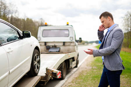 Man calling while tow truck picking up his broken carの写真素材