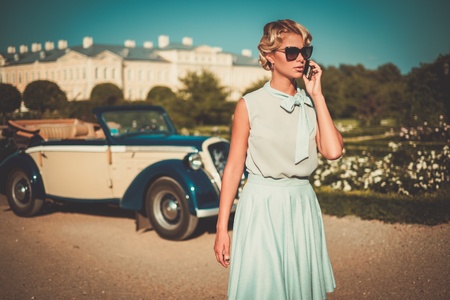 Beautiful lady with mobile phone near classic convertibleの写真素材