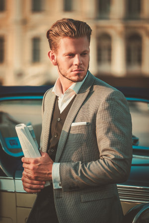 Confident wealthy young man with newspaper near classic convertibleの写真素材