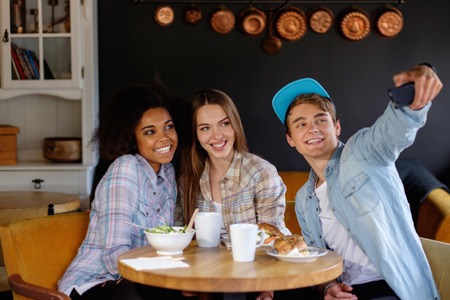 Cheerful multiracial friends taking selfie in a cafeの写真素材