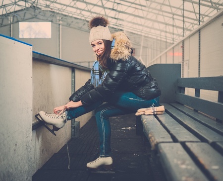 Cheerful girl putting on skates  on ice skating rinkの写真素材