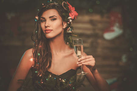 Woman in christmas tree dress in wooden interior with glass of champagneの写真素材