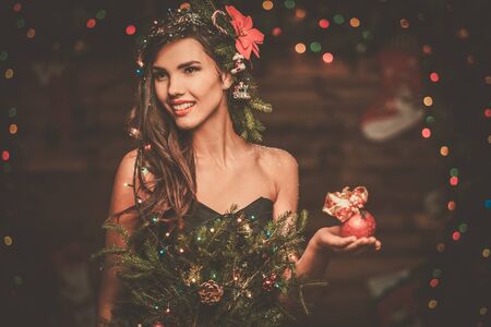 Woman in christmas tree dress in wooden interior holding christmas toyの写真素材