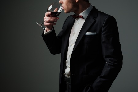 Sharp dressed man wearing jacket and bow tie with glass of vineの写真素材