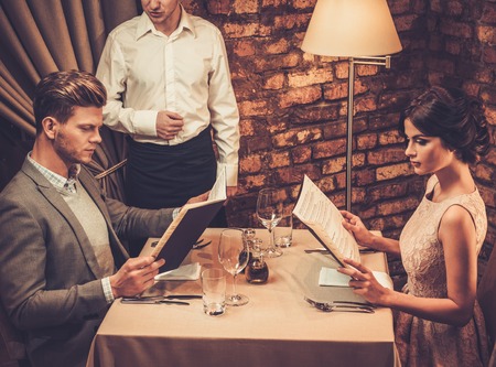 Waiter explaining the menu to stylish wealthy couple in restaurant.の写真素材
