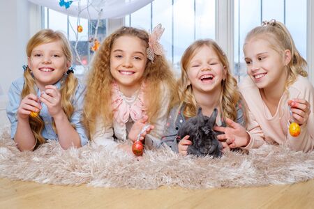 Group of beautiful little girls lying on carpet and playing with cute bunny.の写真素材