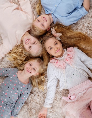 Group of beautiful little girls lying head to head on carpet.の写真素材