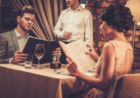 Waiter explaining the menu to stylish wealthy couple in restaurant.の写真素材