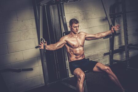 Athletic man doing exercises on training apparatus at the gym's studio