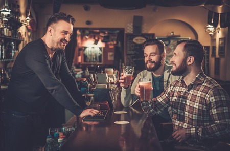 Cheerful old friends drinking draft beer at bar counter in pub.