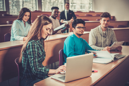 Multinational group of cheerful students taking an active part in a lesson while sitting in a lecture hall.