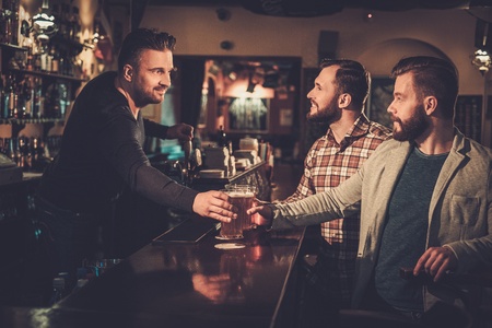 Cheerful old friends drinking draft beer at bar counter in pub.の写真素材