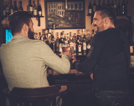 Cheerful old friends drinking draft beer at bar counter in pub.
