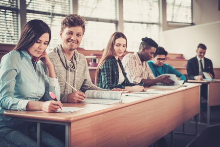 Multinational group of cheerful students taking an active part in a lesson while sitting in a lecture hall.の写真素材