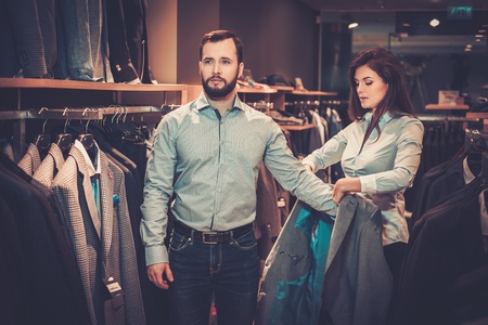 Confident handsome man with beard choosing a jacket in a suit shop.の写真素材