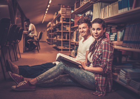 Young couple of cheerful students sitting on the floor and studying in the university library.の写真素材