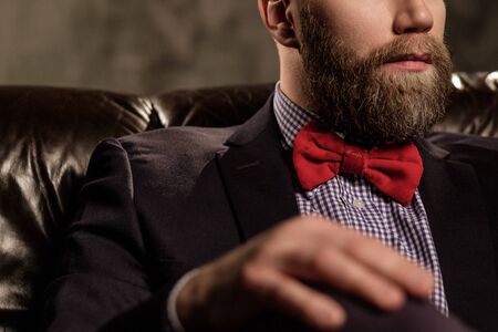 Old-fashioned bearded man sitting in comfortable leather sofa isolated on gray.の写真素材