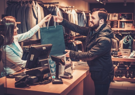 Happy handsome man taking shopping bag from saleswoman in a suit shop.の写真素材