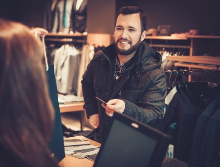Happy handsome man taking shopping bag from saleswoman in a suit shop.の写真素材