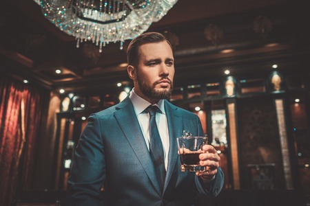 Confident well-dressed man with glass of whisky in luxury apartment interior.の写真素材