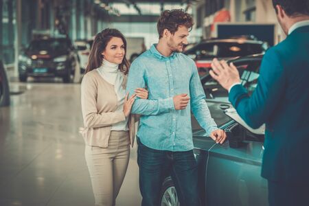 Salesman talking to a young couple at the dealership showroom.の写真素材