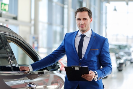 Confident young car dealer standing in showroom.の写真素材