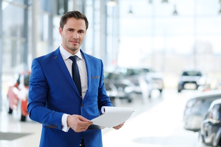 Confident young car dealer standing in showroom.の写真素材