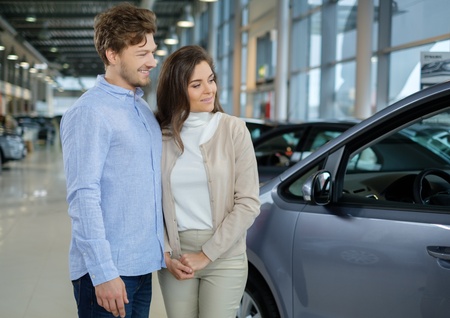 Beautiful young couple looking a new car at the dealership showroom.の写真素材
