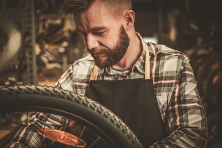 Stylish bicycle mechanic doing his professional work in workshop.の写真素材