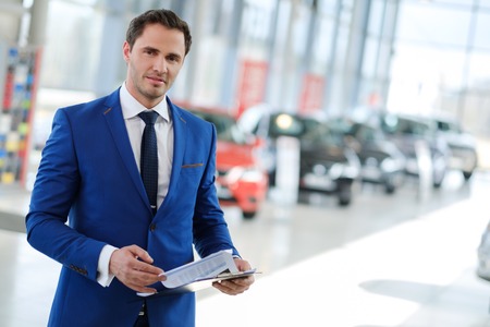 Confident young car dealer standing in showroom.の写真素材