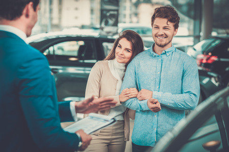 Salesman talking to a young couple at the dealership showroom.の写真素材