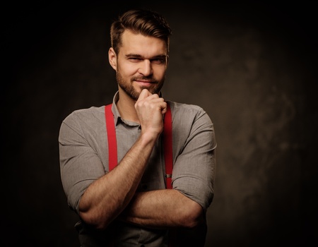 Young handsome man with beard wearing suspenders and posing on dark background.の写真素材