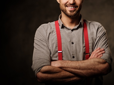 Young handsome man with beard wearing suspenders and posing on dark background.の写真素材
