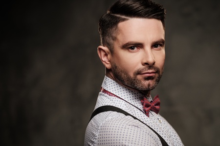 Stylish man with bow tie wearing suspenders and posing on dark background.の写真素材
