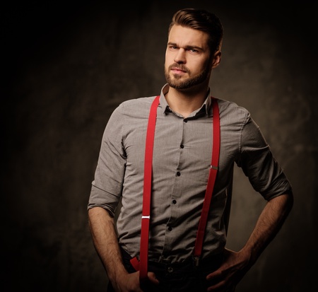 Young handsome man with beard wearing suspenders and posing on dark background.の写真素材