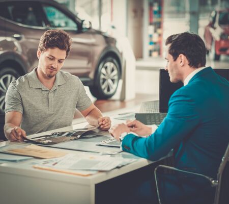 Handsome young man reading a booklet at the dealership showroom.の写真素材